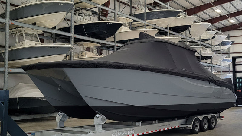 Large covered boat on a trailer inside a warehouse with other boats in the background.